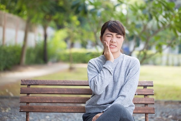 Woman with jaw pain, sitting on a park bench