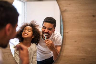 Father and daughter brushing teeth in front of bathroom mirror
